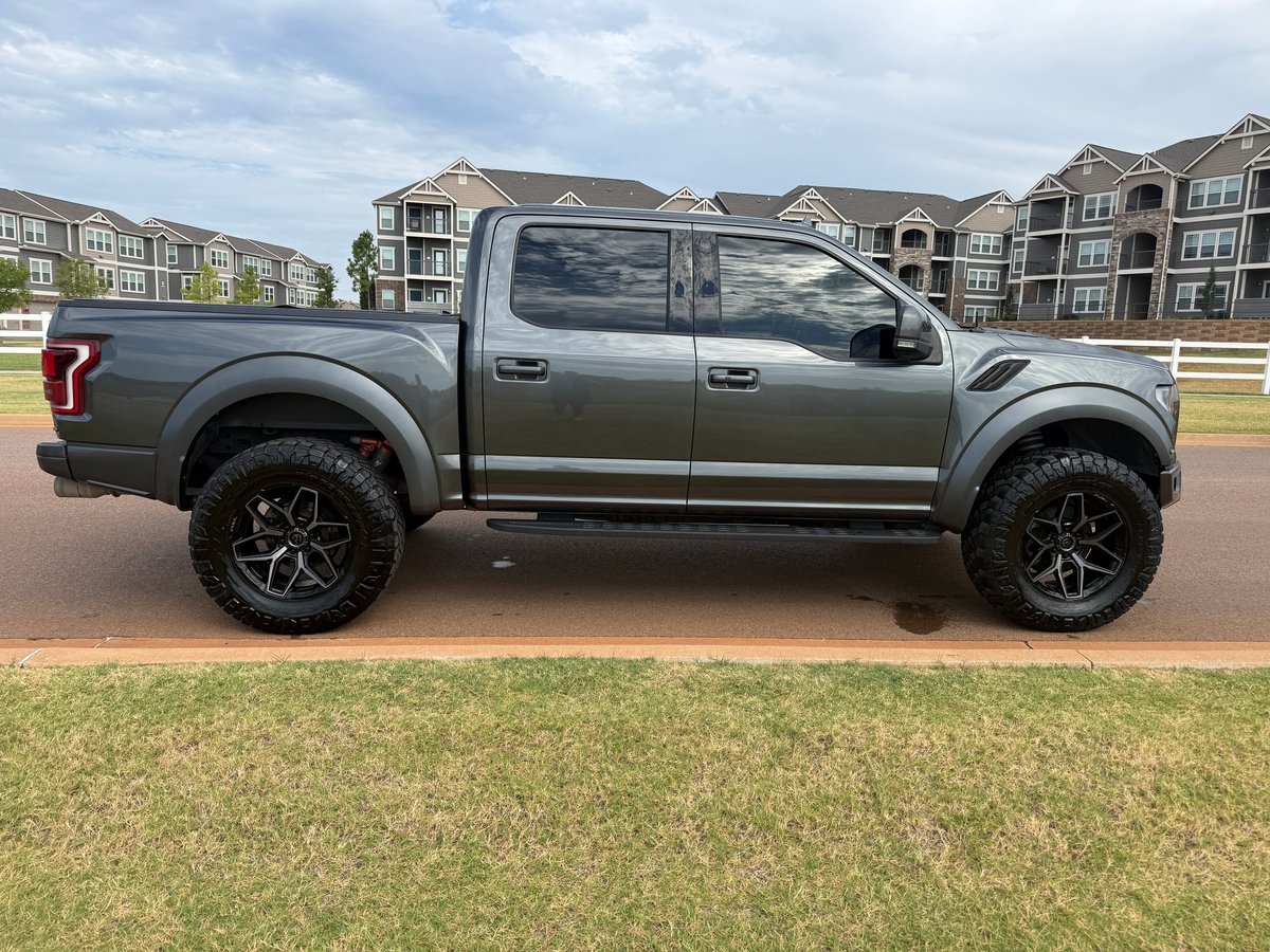 Gray lifted pickup truck with custom wheels parked on grass in a suburban neighborhood