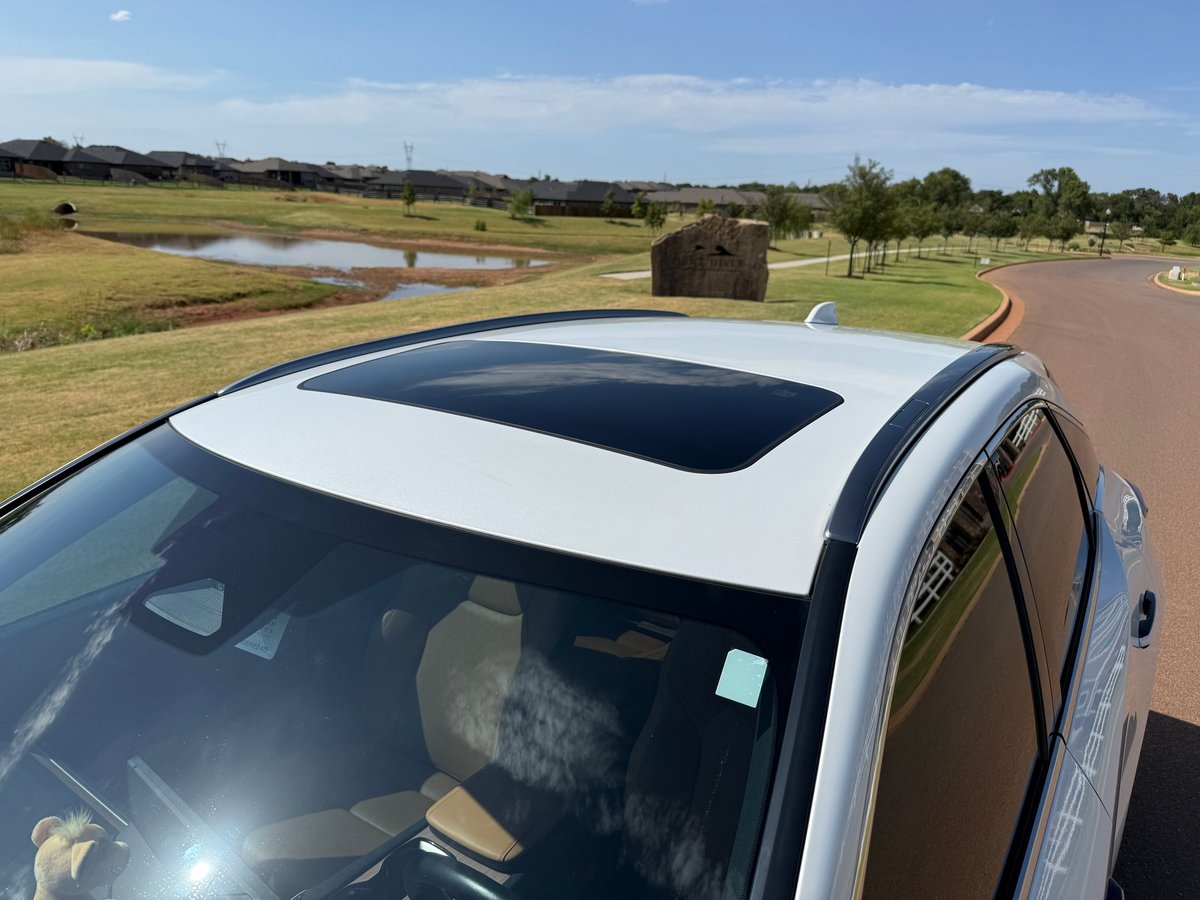 Overhead view of a white SUV with an open panoramic sunroof, parked in a rural countryside with green fields in the background