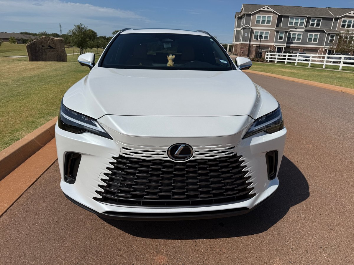 White Lexus sedan parked on a driveway after a full detail, with a large house and green lawn in the background