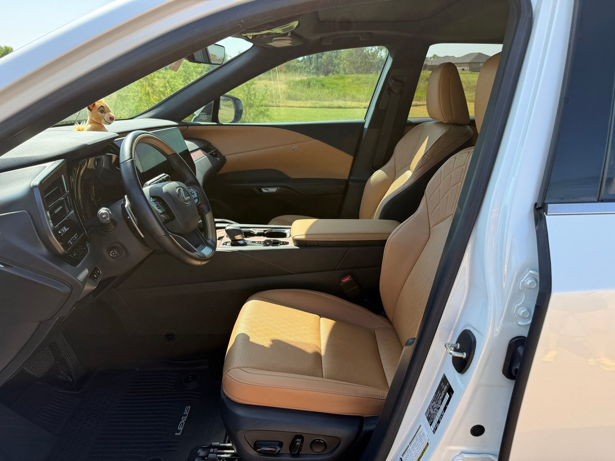 Interior view of a modern SUV with tan and black leather seats, black steering wheel, and dashboard visible through the open driver's-side door