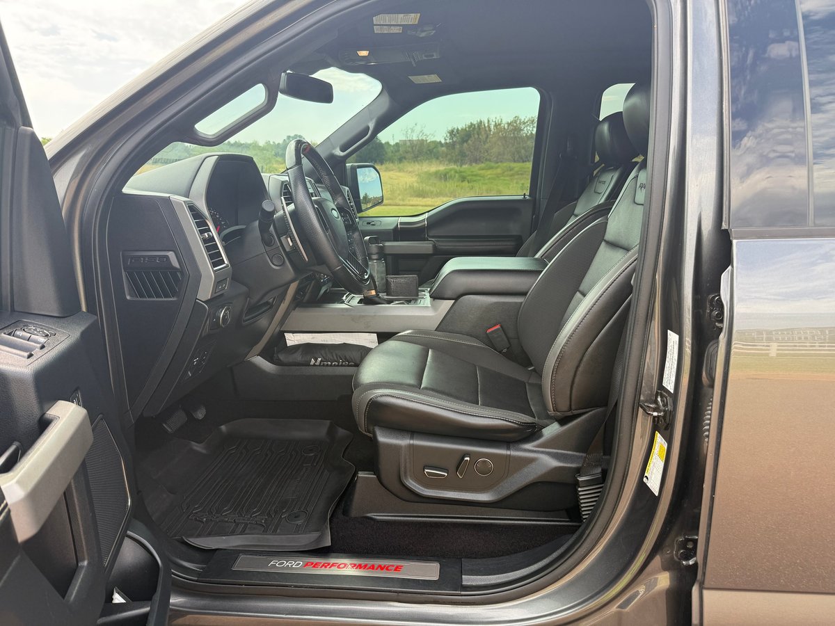 Truck cab interior with black leather seats, steering wheel, and dashboard with rural landscape visible through the windshield